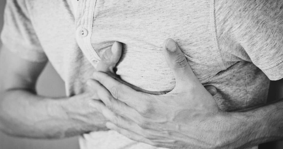 Black and white photo of a man clutching his chest, indicating discomfort or pain.