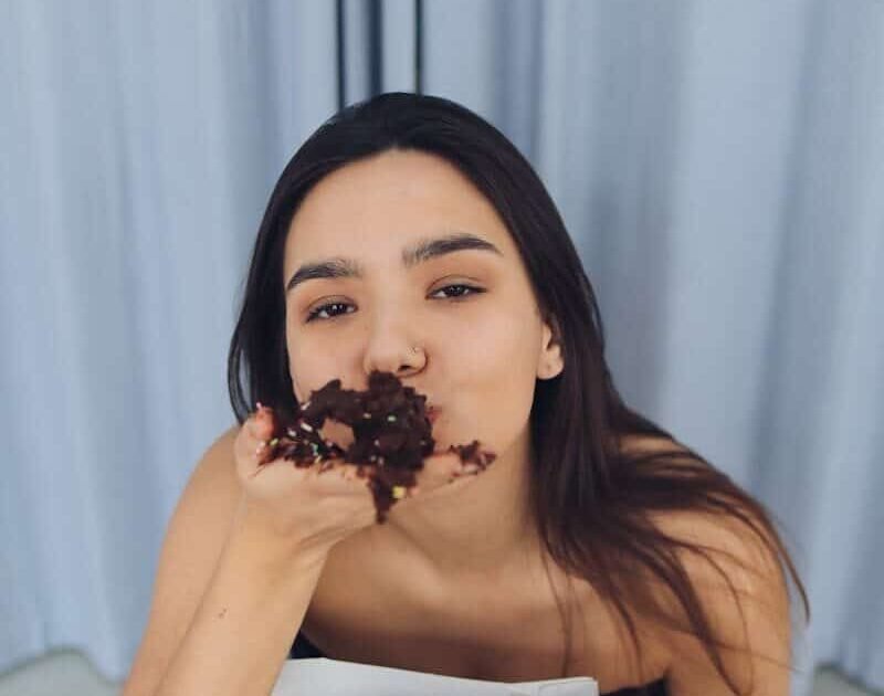 A young woman enjoying chocolate cake in a relaxed indoor setting.