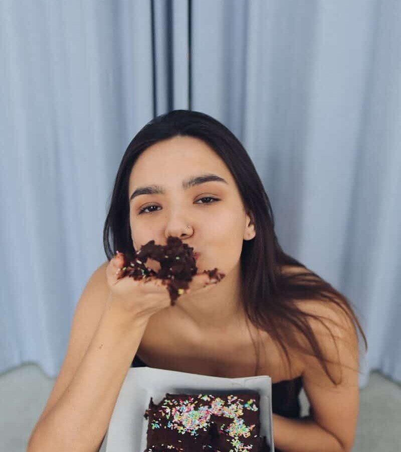 A young woman enjoying chocolate cake in a relaxed indoor setting.