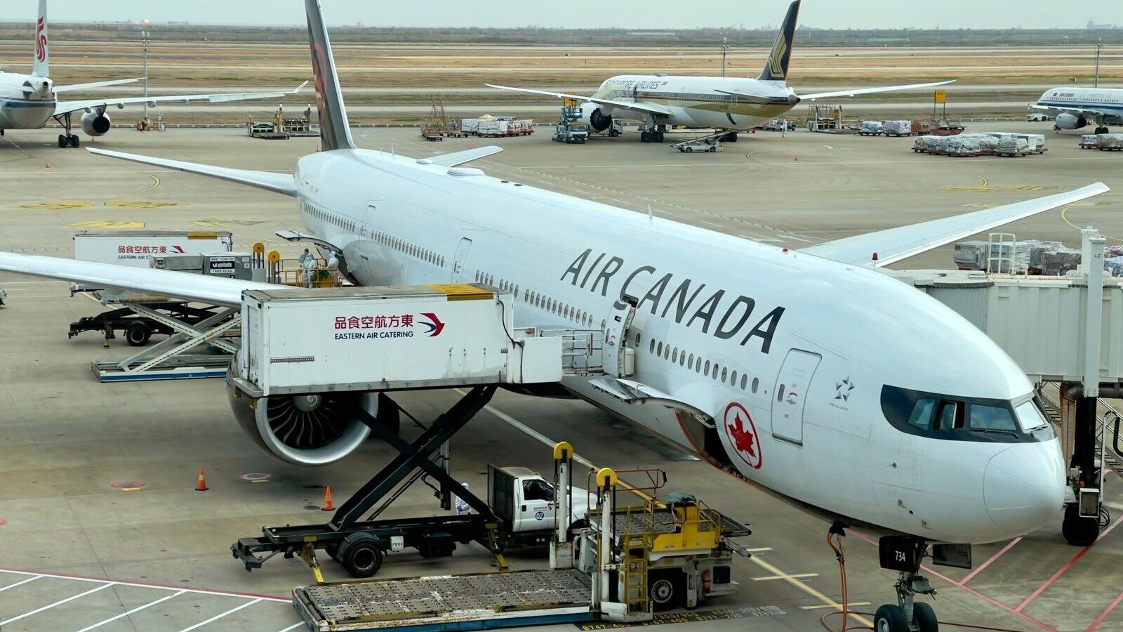 Air Canada airplane being serviced at Shanghai Pudong Airport. Busy tarmac with multiple aircraft.