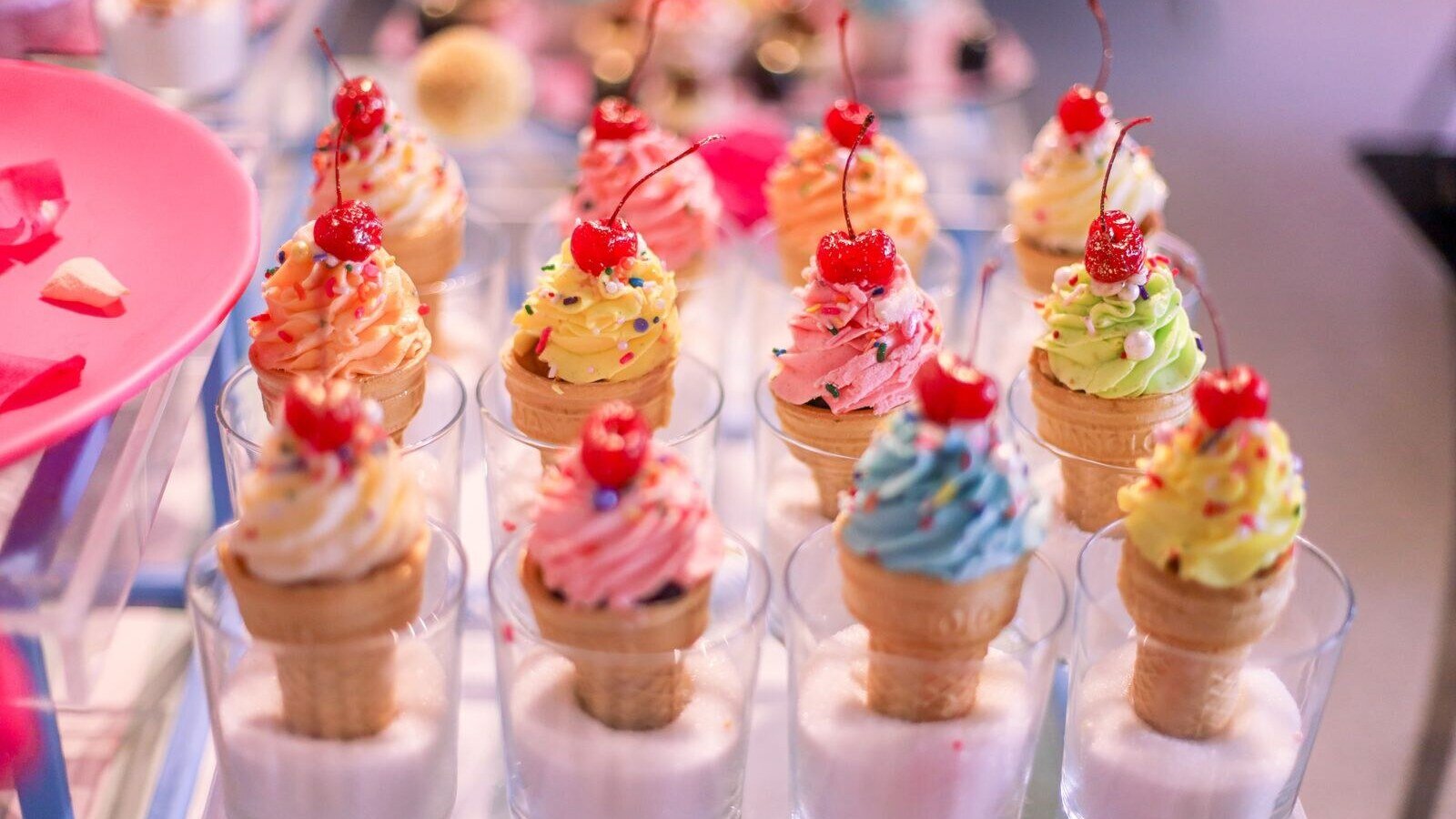 Vibrant ice cream cones with cherries and sprinkles in glass cups, perfect for a sweet treat.