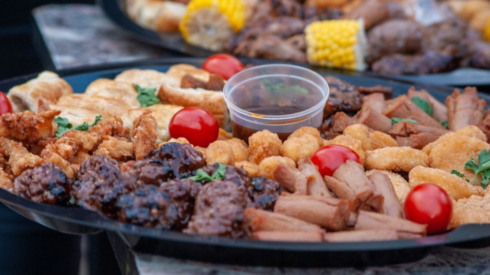 Close-up of a delicious snack platter featuring cherry tomatoes, chicken nuggets, sausages, and corn.