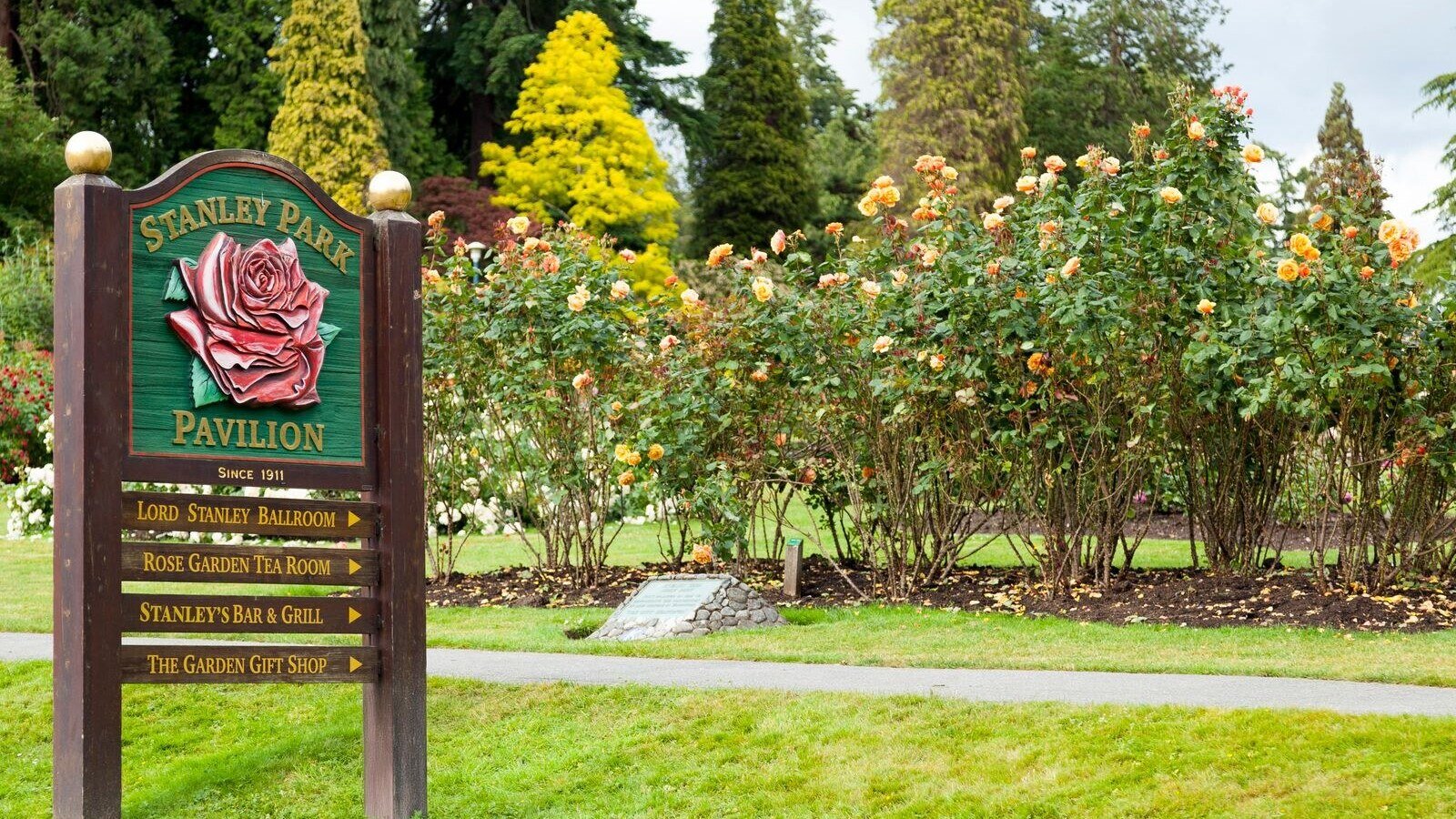 Beautiful Stanley Park Rose Garden with pavilion sign in Vancouver, displaying colorful roses and lush greenery.