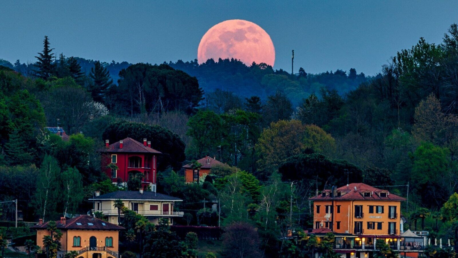 Full moon rises over a lush village with colorful houses and dense greenery.