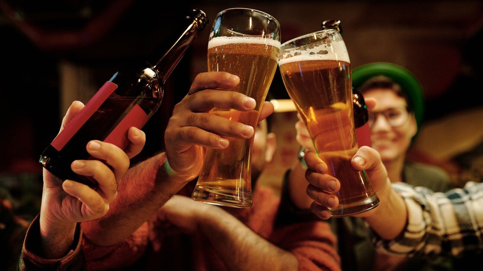 Cheerful group of friends toasting with beer glasses in a lively pub setting.