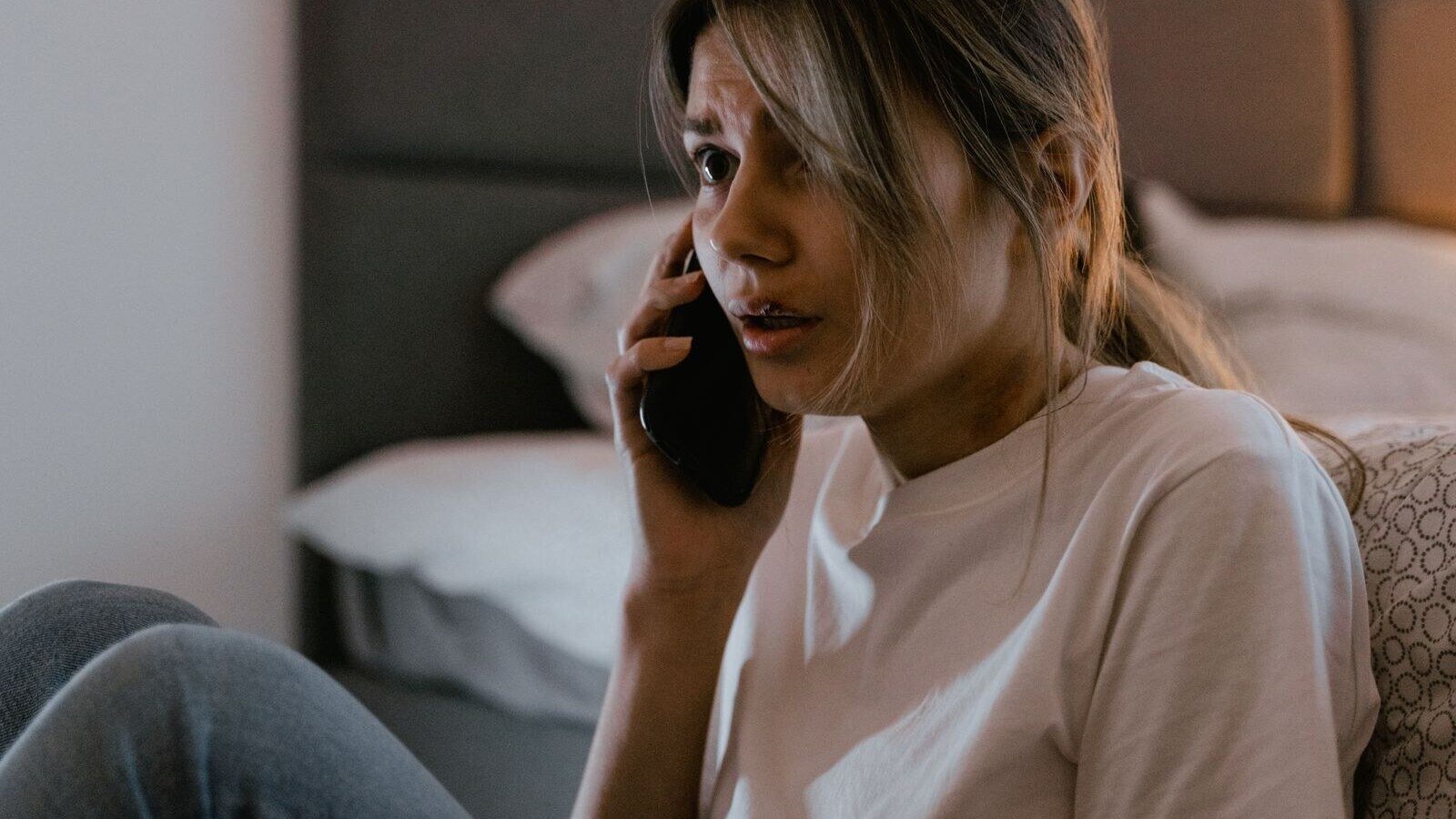 A worried woman in a white shirt making a distressing phone call indoors.