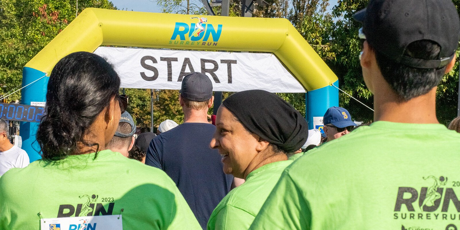 Runners in lime RunSurreyRun shirts stand under a yellow and blue inflatable START arch at Holland Park in Surrey